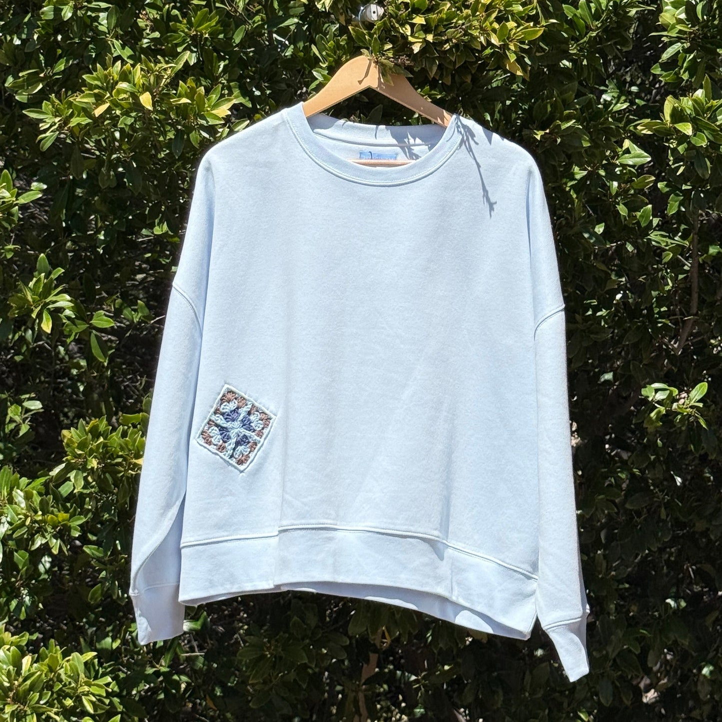 Light blue sweatshirt hanging on a hanger against a green leafy background