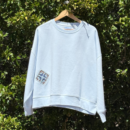 Light blue sweatshirt hanging on a hanger against a green leafy background